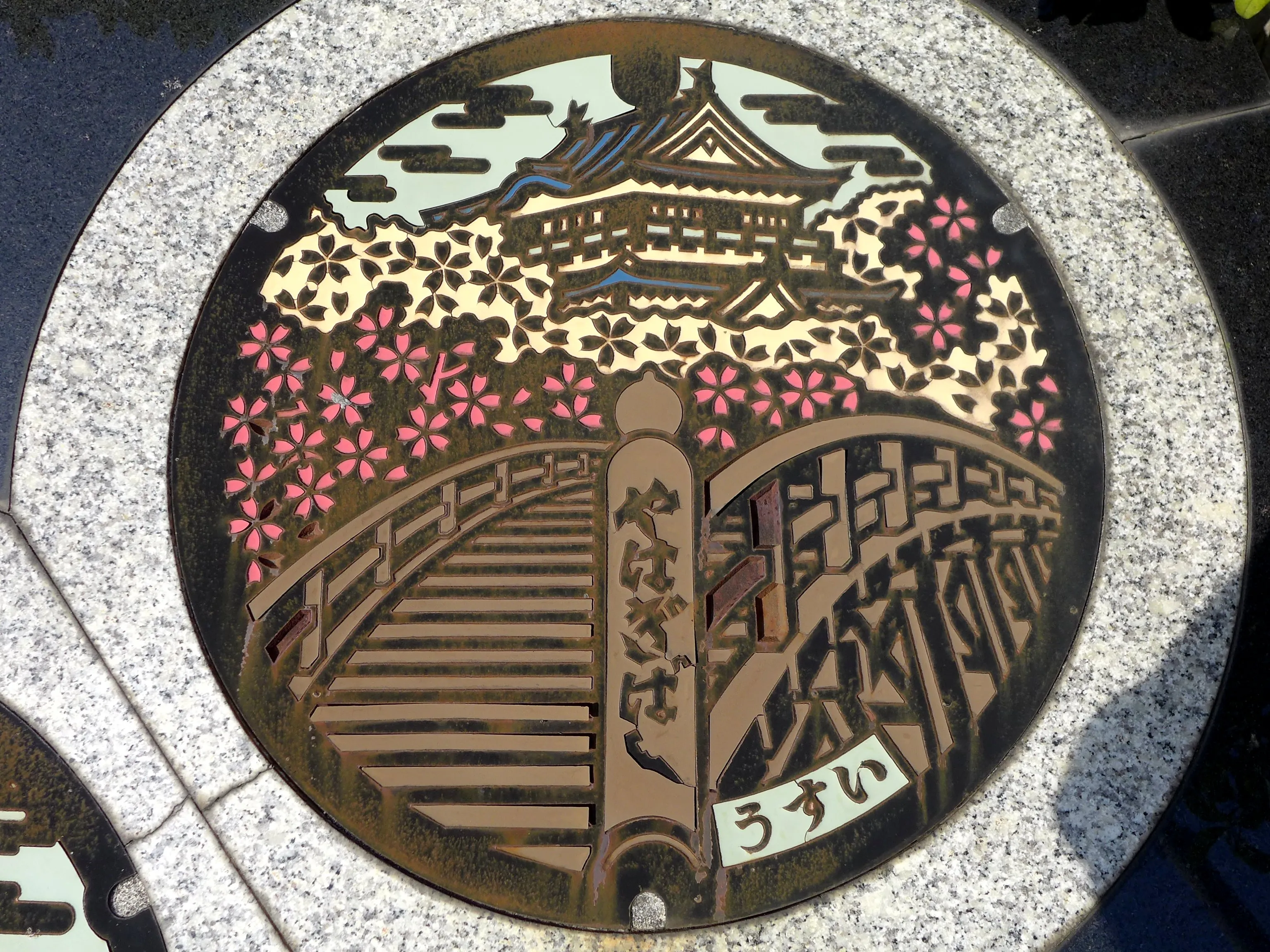 Manhole cover in Okazaki, Aichi, showing Okazaki Castle and cherry blossom above an arched bridge